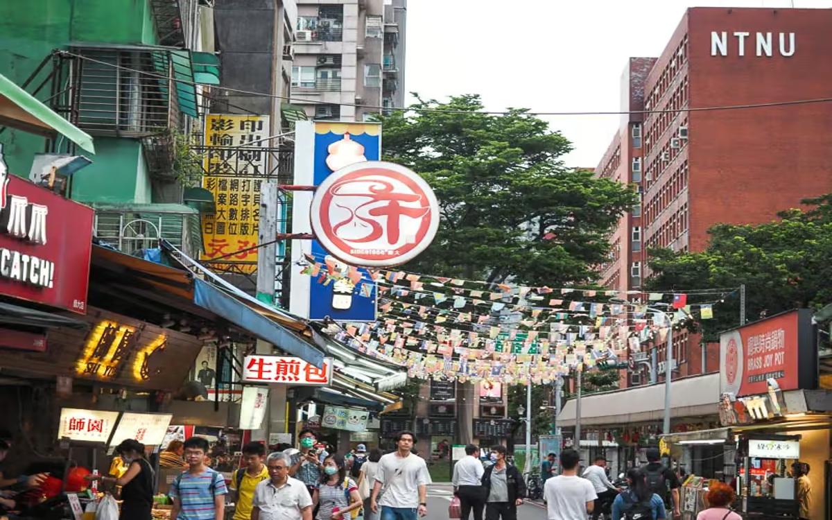 Chợ đêm Đài Bắc với các gian hàng ẩm thực đường phố sáng đèn và nhiều người đi bộ.